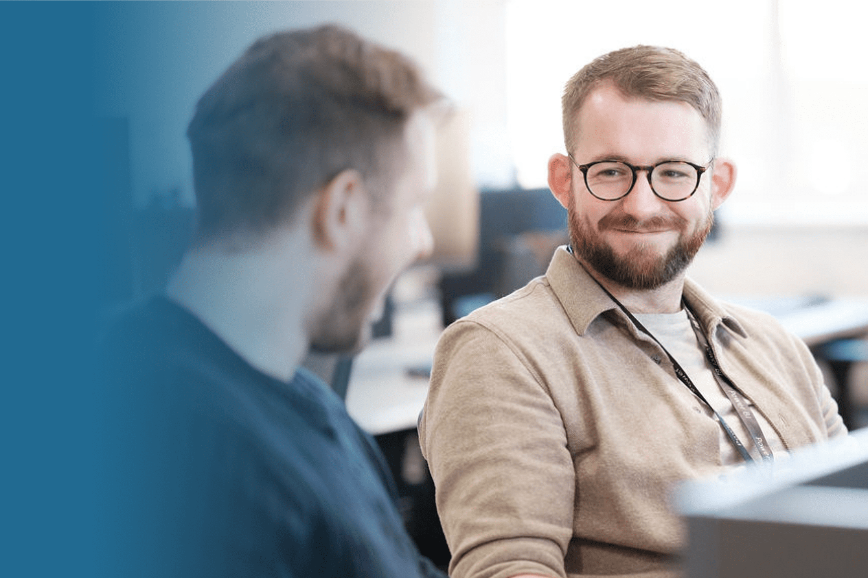 two office workers sat at their desk, smiling and talking.
